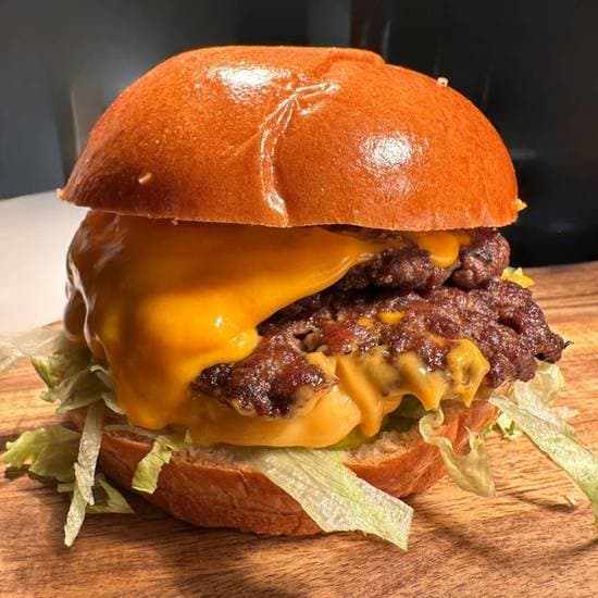 A double smashed cheeseburger with crisp edges and sriracha mayo on branded Fuegos paper