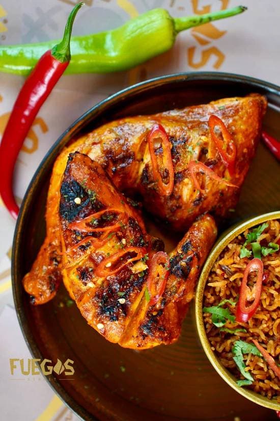 Charred peri-peri half chicken on a bed of rice, scattered with fresh red chilli